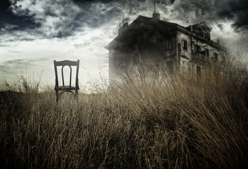 Abandoned chair out in a field facing a haunted house